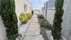 A narrow stone pathway flanked by buildings with white walls and green shrubs. - Modern house with terrace and parking. Overlooking the city (Clermont-Ferrand)