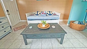 Una habitación con una cama, una mesa de madera oscura con cajones, una planta en maceta y un estante fijado a la pared.