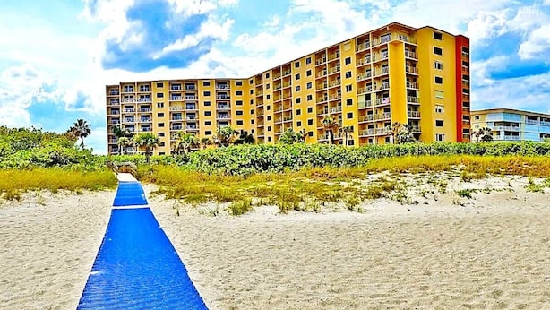 Un hotel frente a la playa con un camino azul que conduce al edificio, rodeado de vegetación.