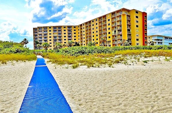 A beachfront hotel with a blue pathway leading to the building, surrounded by greenery.