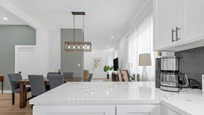 Una cucina moderna con mobili bianchi, un'isola in marmo e una macchina per il caffè.