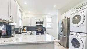 Una cucina moderna con mobili bianchi, un'isola centrale, elettrodomestici in acciaio inossidabile e lavatrice e asciugatrice integrate.