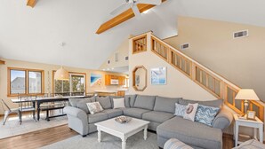 Ein geräumiges Wohnzimmer mit einem großen Ecksofa, einem Esstisch und einer Treppe.