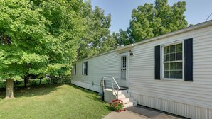 A single-story mobile home with a front porch, a small set of steps, and a garden area with a tree and flowers. - Serene Getaway Centrally Located in the FLX (Dundee)