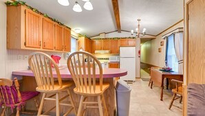 A compact kitchen with wooden cabinets, a central island with chairs, a dining table, and a trash bin. - Serene Getaway Centrally Located in the FLX (Dundee)