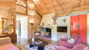 A cozy living room with a fireplace, wooden ceiling beams, and a red door. - Holiday Home 'Eclectic Monte Laginha Alentejo' with Private Pool, Terrace & Wi-Fi (Lajinha)