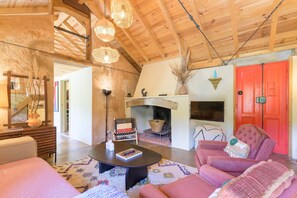 A cozy living room with a fireplace, wooden ceiling beams, and a red door.