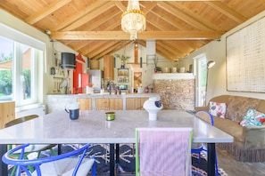 A spacious kitchen with wooden beams, a chandelier, and a stone wall.