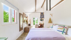 Een slaapkamer met een groot bed, een bureau, een stoel en een raam met uitzicht op groen.