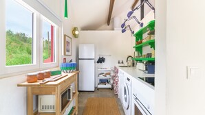Een compacte keuken met een wasmachine, een koelkast en een raam met uitzicht op groen.