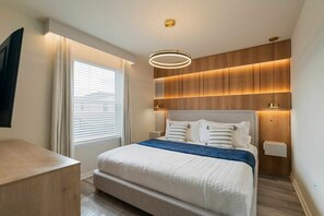 A modern bedroom with a large bed, bedside tables, a built-in wooden panel wall, and a ceiling light fixture. - 10BR Home w/ Pool & Disney Themes (Clermont)
