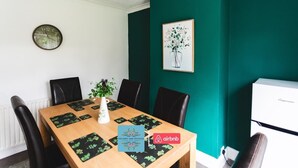 A dining area with a wooden table, black chairs, a clock, a framed artwork, and a white appliance. - 3BR House in Wolves | Ideal for Contractors + Wifi (West Midlands)