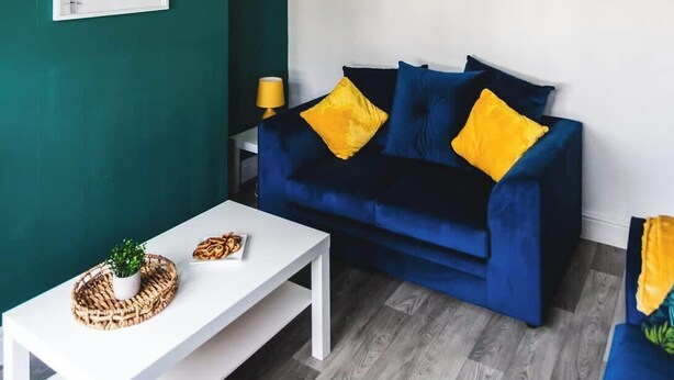 A room with a dark blue sofa, two yellow cushions, a white coffee table, and a small plant. - 3BR House in Wolves | Ideal for Contractors + Wifi (West Midlands)