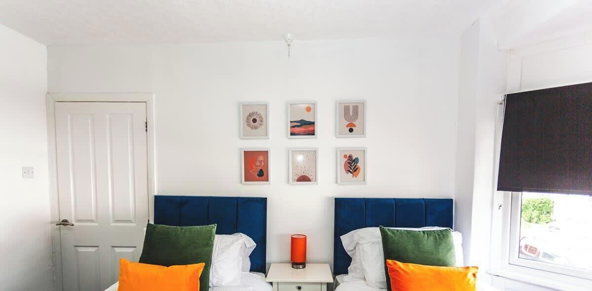 A bedroom with two beds, a nightstand, and six framed pictures on the wall.