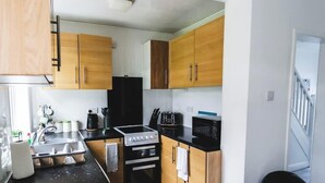 A compact kitchen with wooden cabinets, a black refrigerator, a stove, and a microwave. - 3BR House in Wolves | Ideal for Contractors + Wifi (West Midlands)