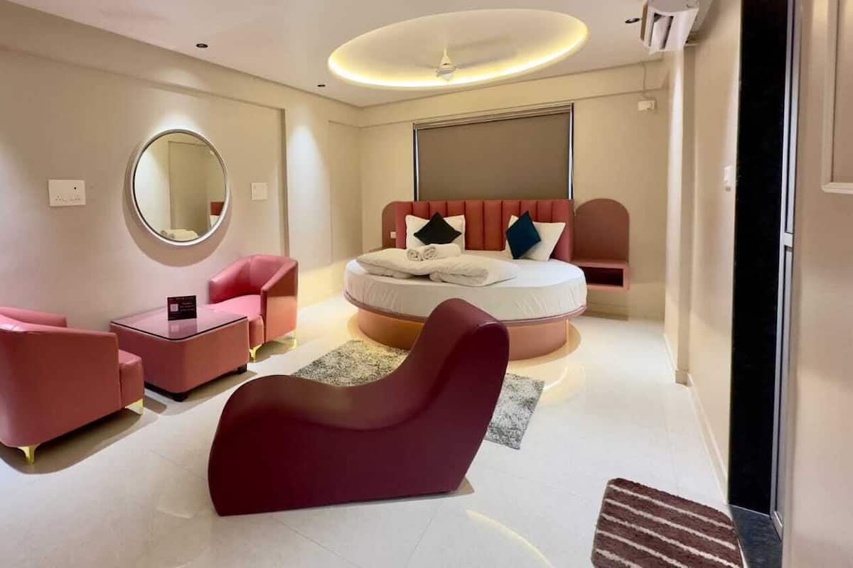 Une chambre d’hôtel moderne avec un lit rond, un miroir rond, un canapé rose et un fauteuil rouge.