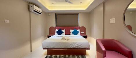 A bedroom with a bed, a red chair, a ceiling fan, and an air conditioning unit.