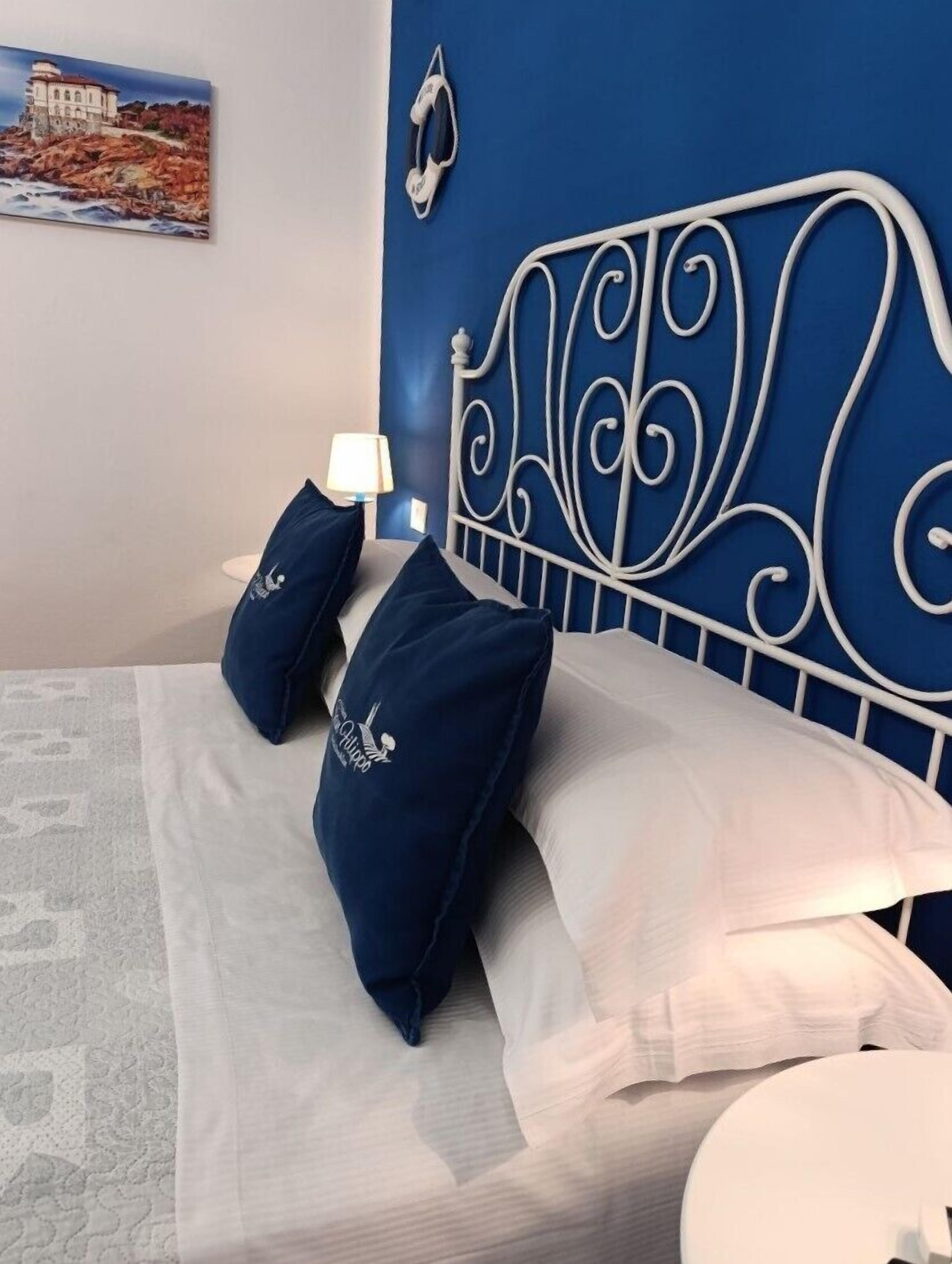 Ein Bett mit weißem Kopfteil und blauen Kissen, eine weiße Lampe und ein Gemälde an der Wand.