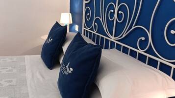 Ein Bett mit weißem Kopfteil und blauen Kissen, eine weiße Lampe und ein Gemälde an der Wand.