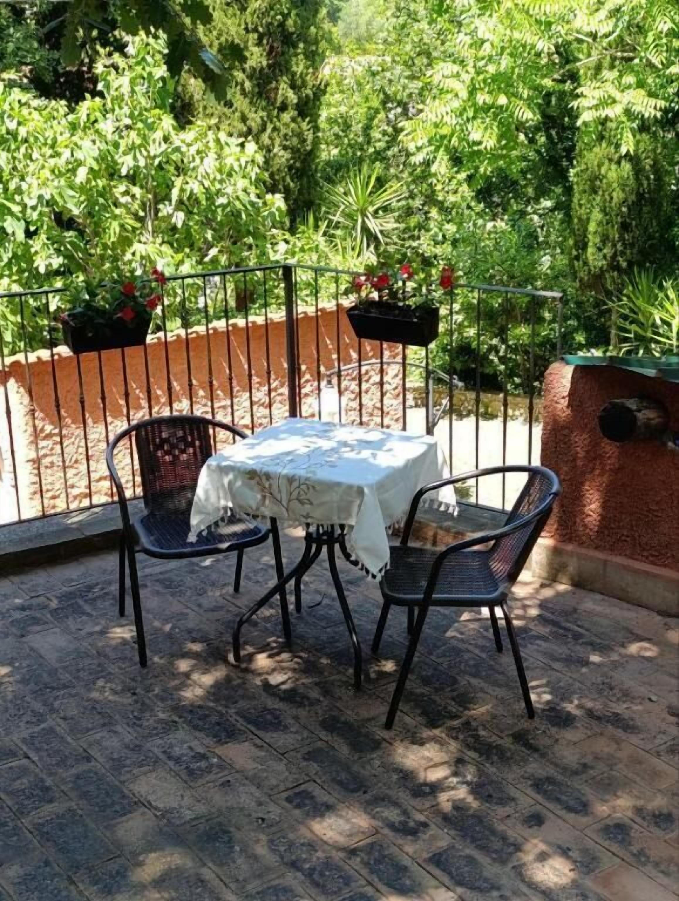 A patio with a table and two chairs, surrounded by a metal fence and potted plants.
