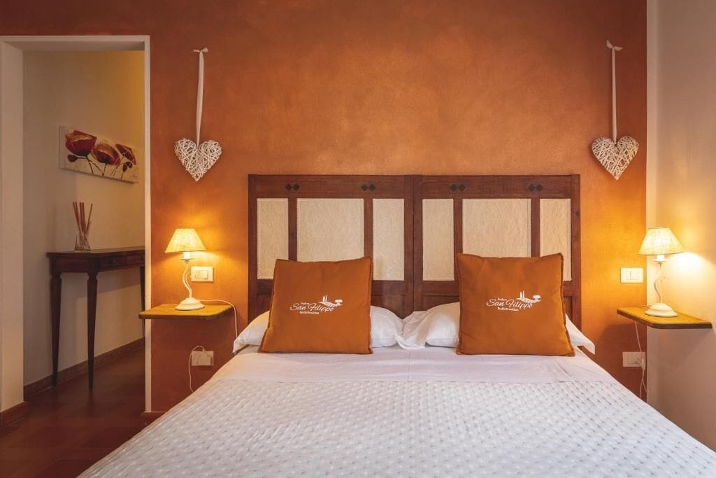 Une chambre d’hôtel avec une tête de lit en bois, deux oreillers ornés de motifs, des lampes de chevet et une décoration en forme de cœur fixée au mur.