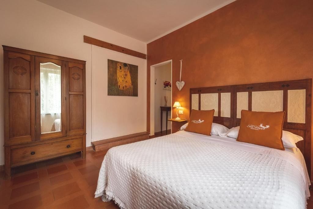 A bedroom with a large bed, wooden wardrobe, and a painting on the wall.