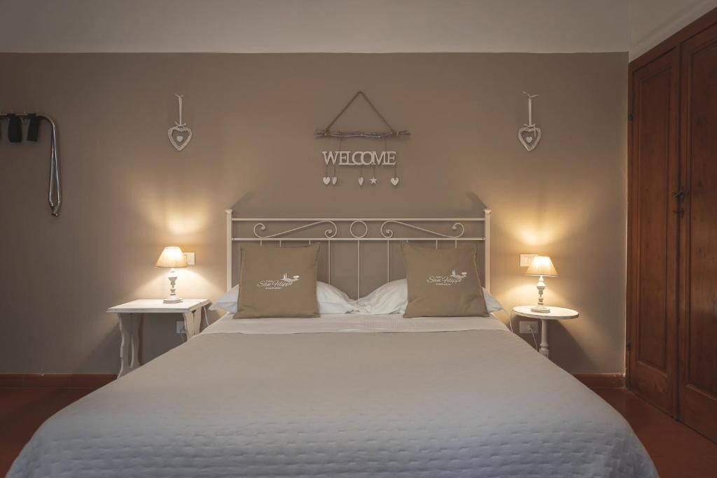 Une chambre d’hôtel avec un grand lit, deux tables de chevet avec des lampes, une pancarte « BIENVENUE » au-dessus du lit et une armoire sur le côté droit.