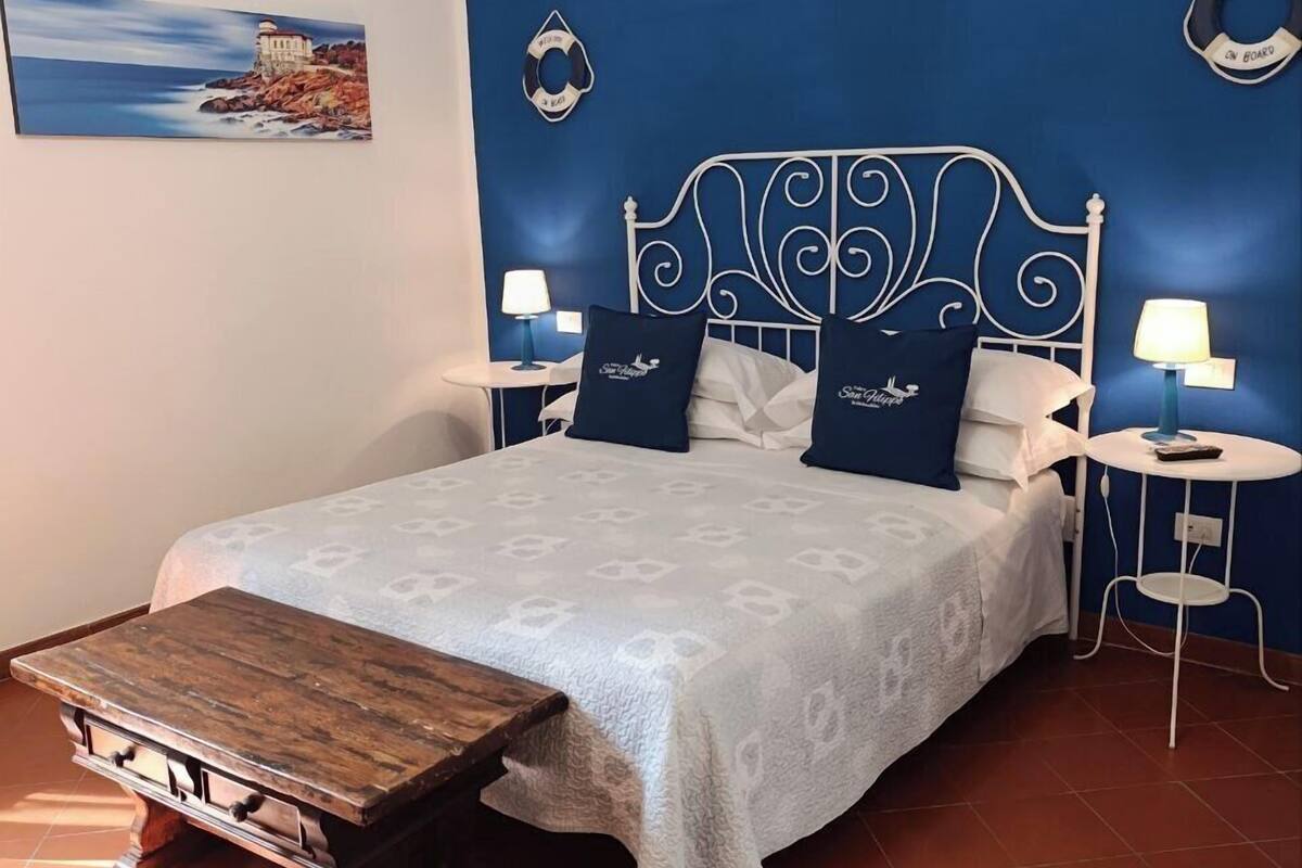 A bed with a white headboard, a wooden bedside table, and a blue wall with a painting and two wall decorations.