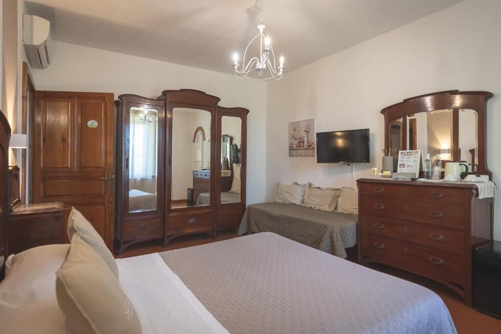 A hotel room with a large bed, wooden wardrobe, a television, and a chandelier.