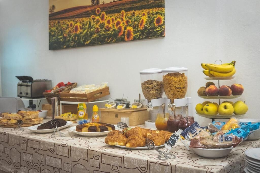 Um buffet de café da manhã com diversos alimentos e uma pintura de um campo de girassóis na parede.