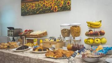Um buffet de café da manhã com diversos alimentos e uma pintura de um campo de girassóis na parede.