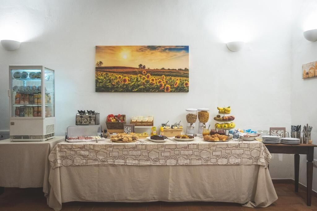 Un tavolo per buffet con diversi cibi, un frigorifero e un dipinto raffigurante un tramonto su un campo.