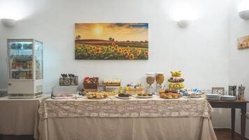 Un tavolo per buffet con diversi cibi, un frigorifero e un dipinto raffigurante un tramonto su un campo.