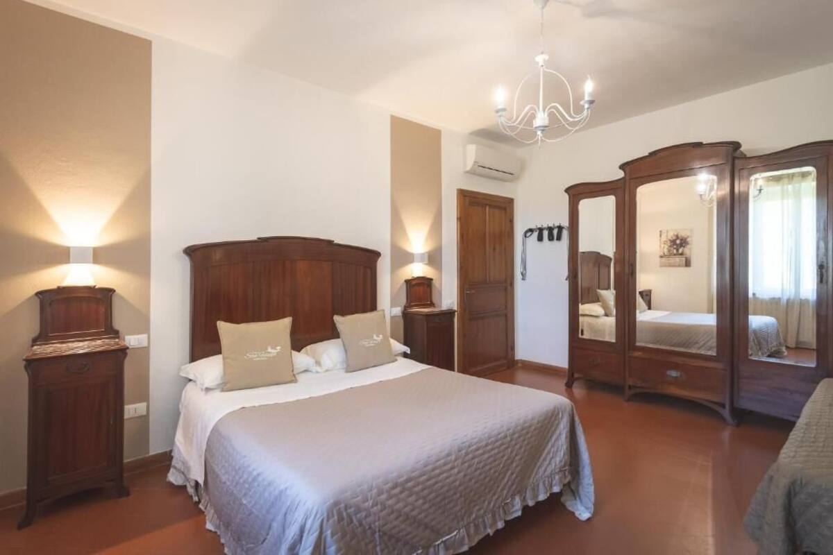 A bedroom with a large bed, wooden wardrobe, and a chandelier.
