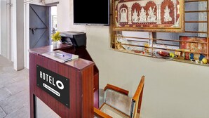 Un comptoir d’accueil d’hôtel avec un téléviseur à écran plat, une image religieuse encadrée et une chaise.