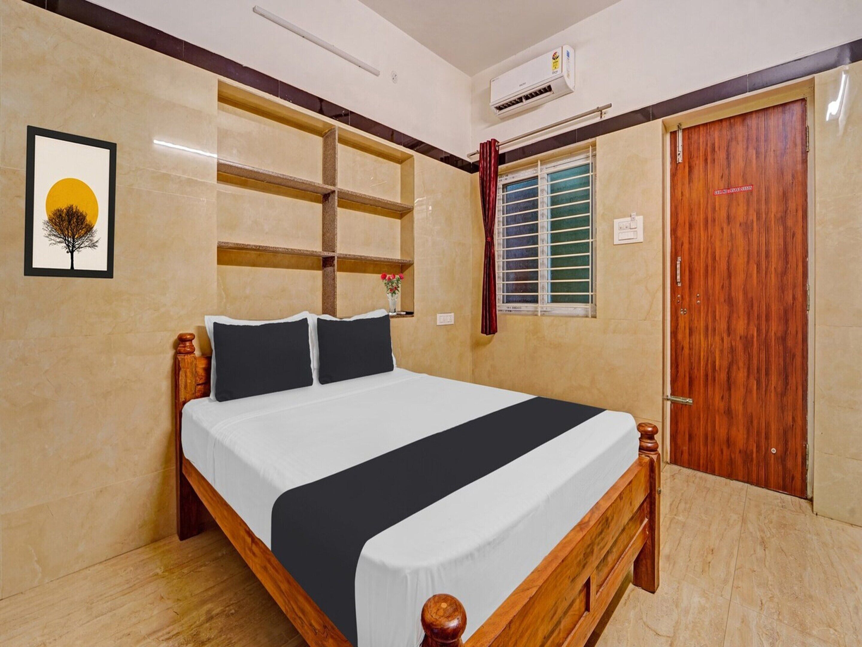 A bedroom with a bed, a wooden headboard, a wall-mounted shelf, a window with a curtain, an air conditioning unit, and a door.