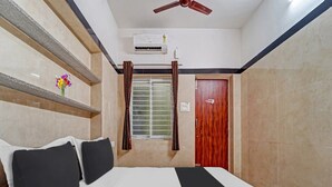 Une chambre d’hôtel équipée d’un lit, d’un ventilateur de plafond, d’un appareil de climatisation, d’une fenêtre avec des rideaux et d’une porte en bois.