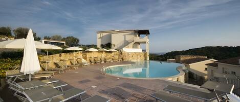 Área de piscina en la azotea con sillones de descanso y sombrillas, una piscina y vistas del paisaje circundante.