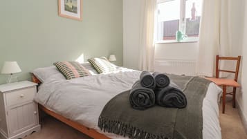 A bedroom with a bed, a nightstand, a chair, a window with curtains, and a framed picture on the wall.