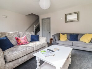 A living room with two sofas, a coffee table, a staircase, and a door. - Mallard Cottage (Driffield)
