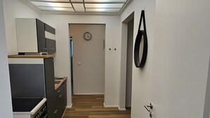 Kapea käytävä, jonka toisella puolella on keittiö, toisella puolella ovi, jossa on kello, ja seinällä pyöreä koriste.