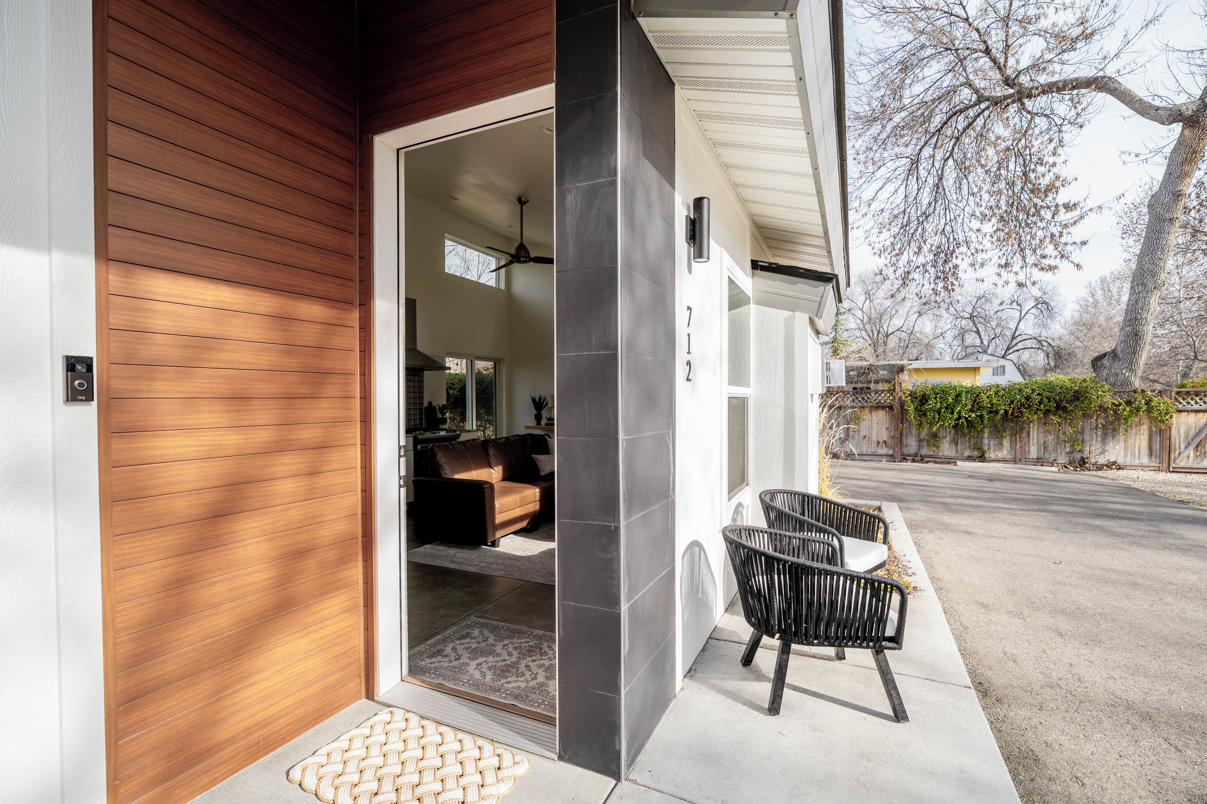 A modern house with a wooden exterior, a visible number '712' on the wall, and a black chair outside.