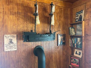 A wooden wall with a ship model, a wanted poster, and a bookshelf with books. - Albert's By The Lighthouse: Historic Home with Modern Updates (Ocracoke)