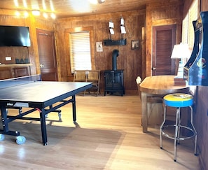 Una habitación con mesa de ping pong, paredes de madera, una zona de bar y una pequeña mesa con taburetes.