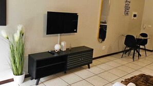 Un soggiorno moderno con una televisione a schermo piatto, un mobile TV nero, uno specchio, un'area pranzo con sedie e un tappeto marrone.