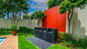 Un cortile con piscina, un muro rosso e un fioriere nero pieno di piante.