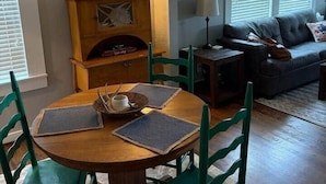 A dining area with a round table and chairs, a wooden cabinet with shelves, and a sofa in the background. - The Gates House (Brady)