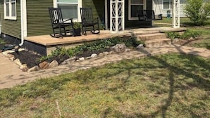 A two-story house with a porch, a small garden, and a clear sky. - The Gates House (Brady)