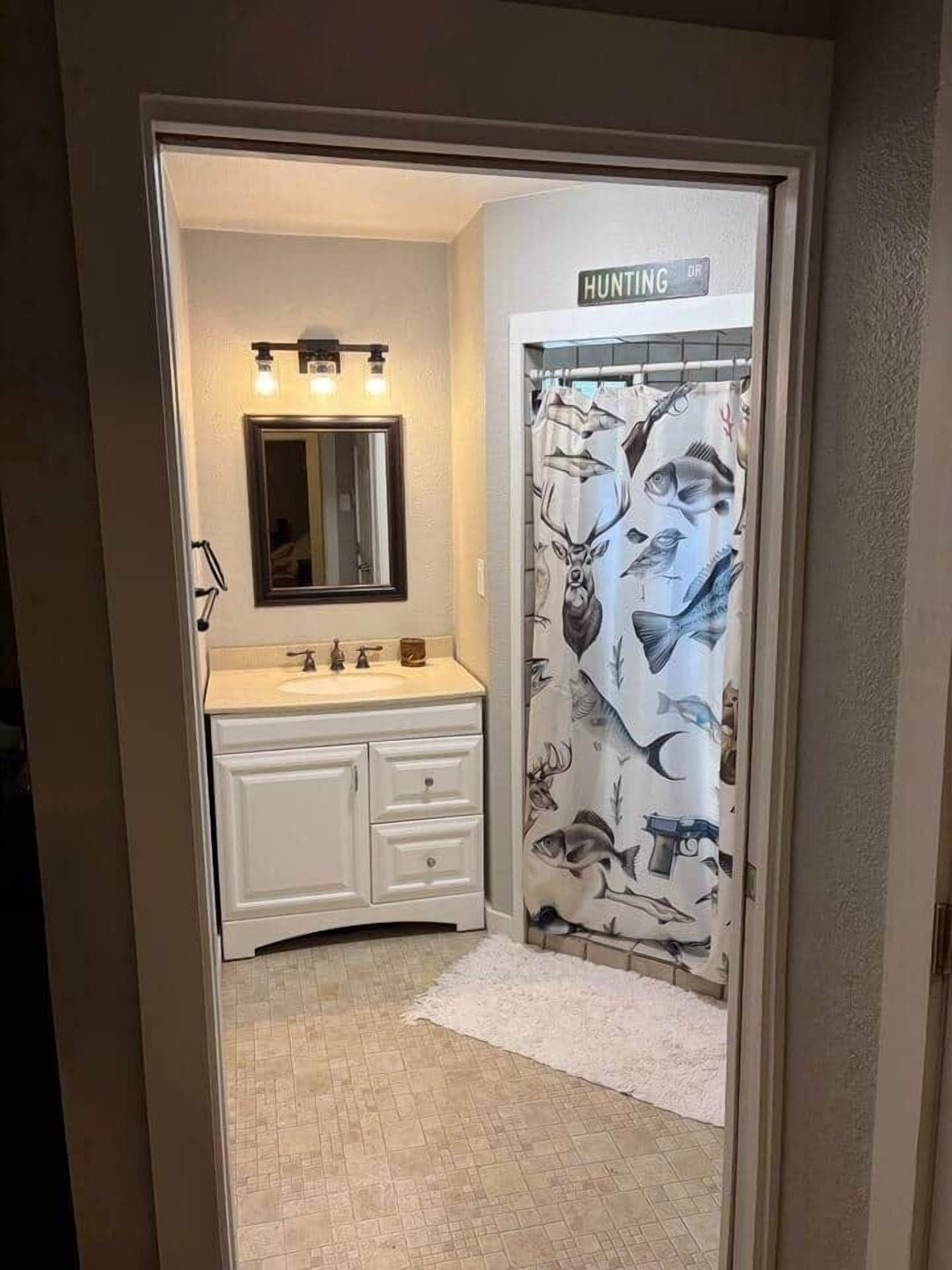 Une salle de bain avec un meuble-lavabo blanc, un miroir et un rideau de douche orné de motifs représentant des animaux sauvages.
