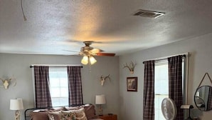 A bedroom with a bed, two bedside tables, a desk, a chair, a ceiling fan, and a window with curtains. - The Gates House (Brady)